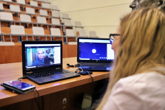 Asystentka wykładowcy, z dwoma laptopami. Na jednym z nich widać prowadzącego zajęcia