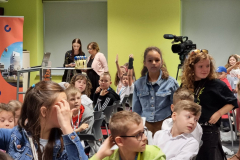 dzieci siedzący na krzesełkach i dwie stojące dziewczynki