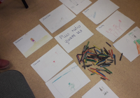 Na środku znajduje się kartka, na której widnieje napis Plus ratio quam vis, dokoła kartki znajdują się prace dzieci