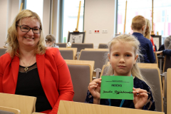 Kobieta w czerwonej marynarce i dziewczynka z indeksem siedzące na auli